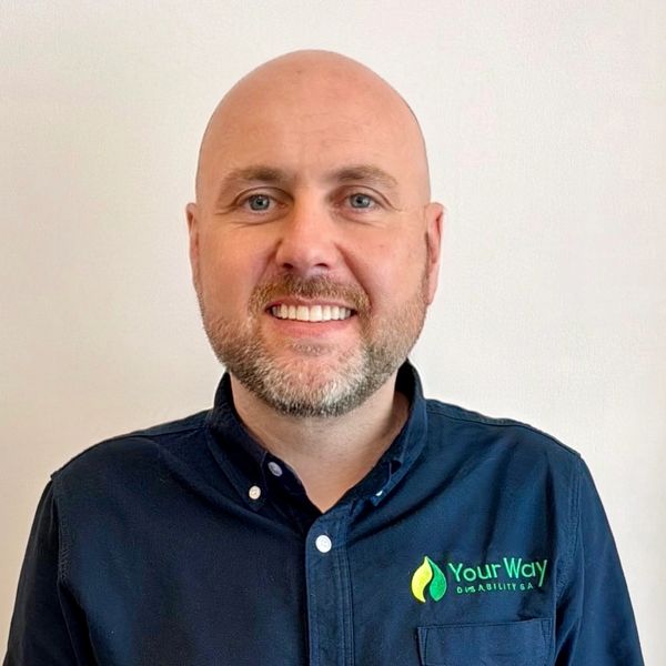 Smiling bald man in a navy shirt with 'Your Way Disability SA' logo.