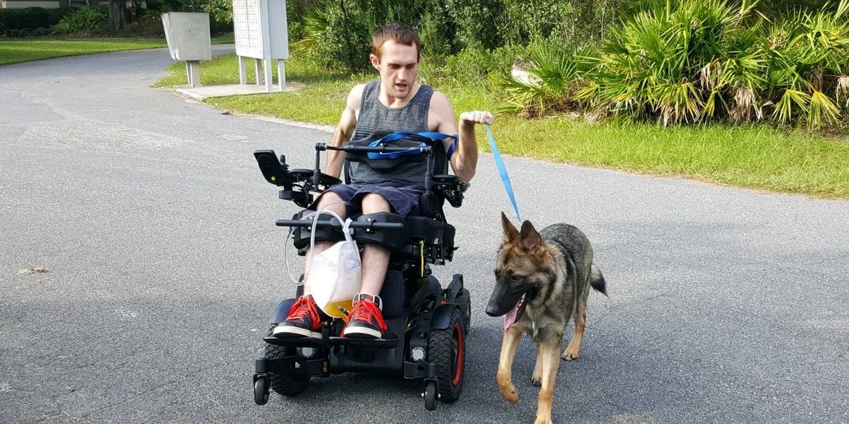 young man in a power wheelchair holding a leash with a german shepherd