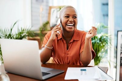 Smiling woman talking on phone while working at laptop.