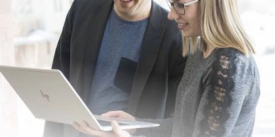 Two professionals smiling while looking at a laptop together.