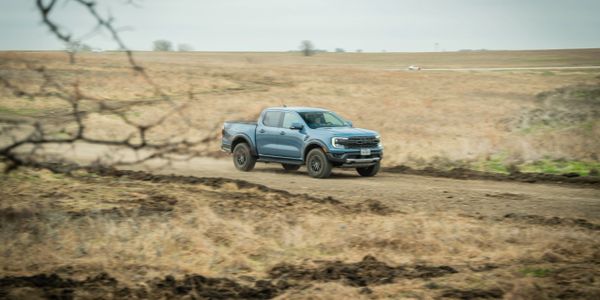 Blue pickup truck driving on a dirt road through a dry field.