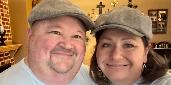 A smiling couple wearing matching gray flat caps indoors.