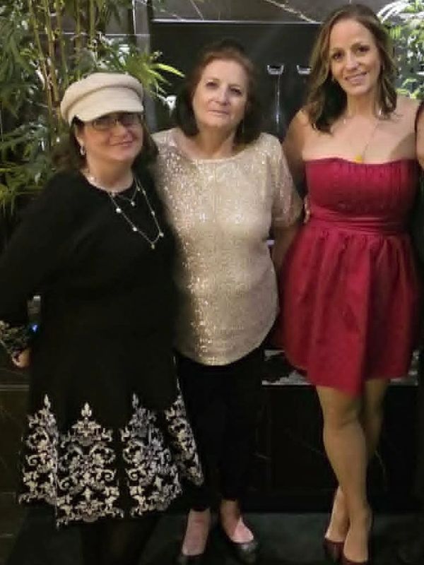 Three women posing together in elegant outfits at an indoor gathering.