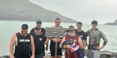 Group of men posing by a sign at the northernmost tip of Australia on a rainy day.