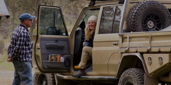 Two people chatting by a rugged off-road vehicle in a forest.