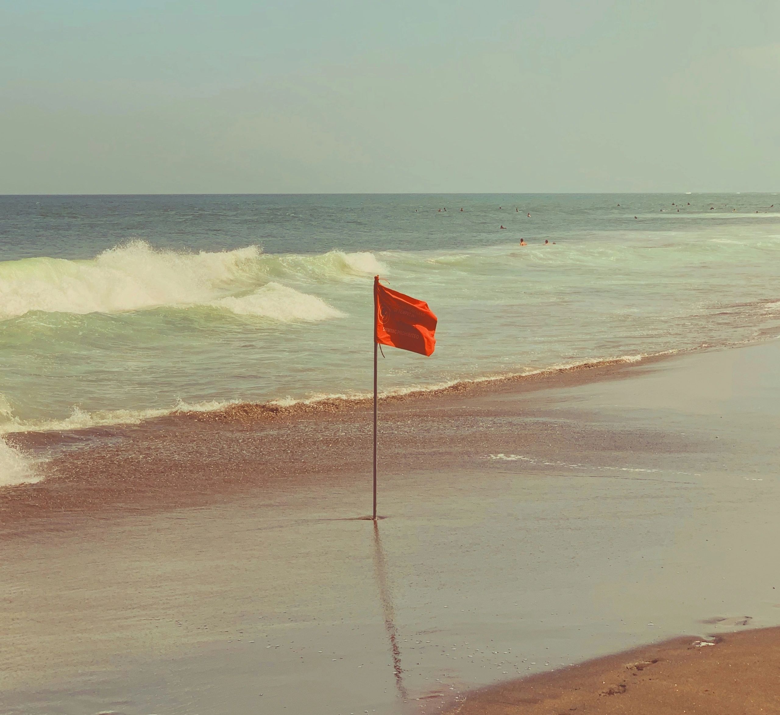 Red warning flag on a beach with waves and swimmers in the background.