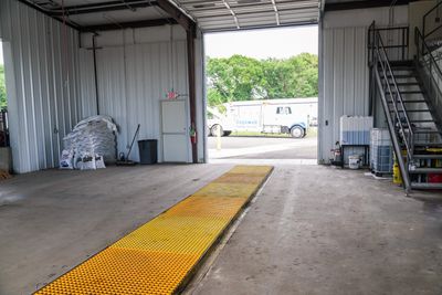 Empty garage with yellow platform and open door showing a tow truck outside.