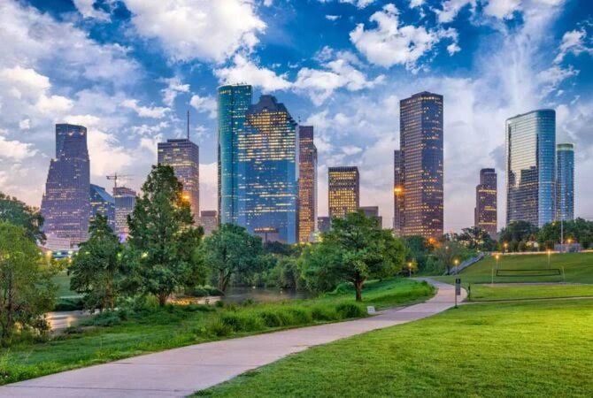 City skyline with modern skyscrapers behind a lush green park path.