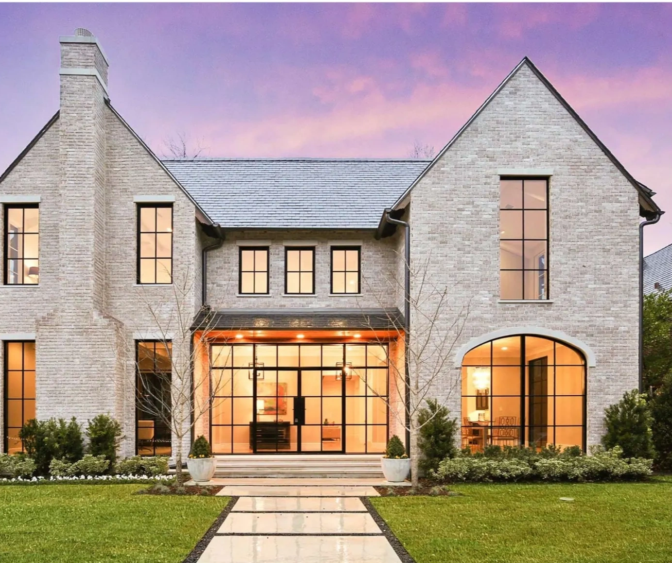 Modern brick house with large windows and a beautiful sunset sky.