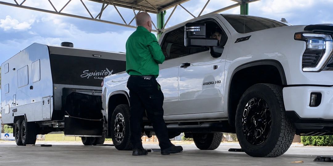 Man talking to driver in white truck towing caravan.