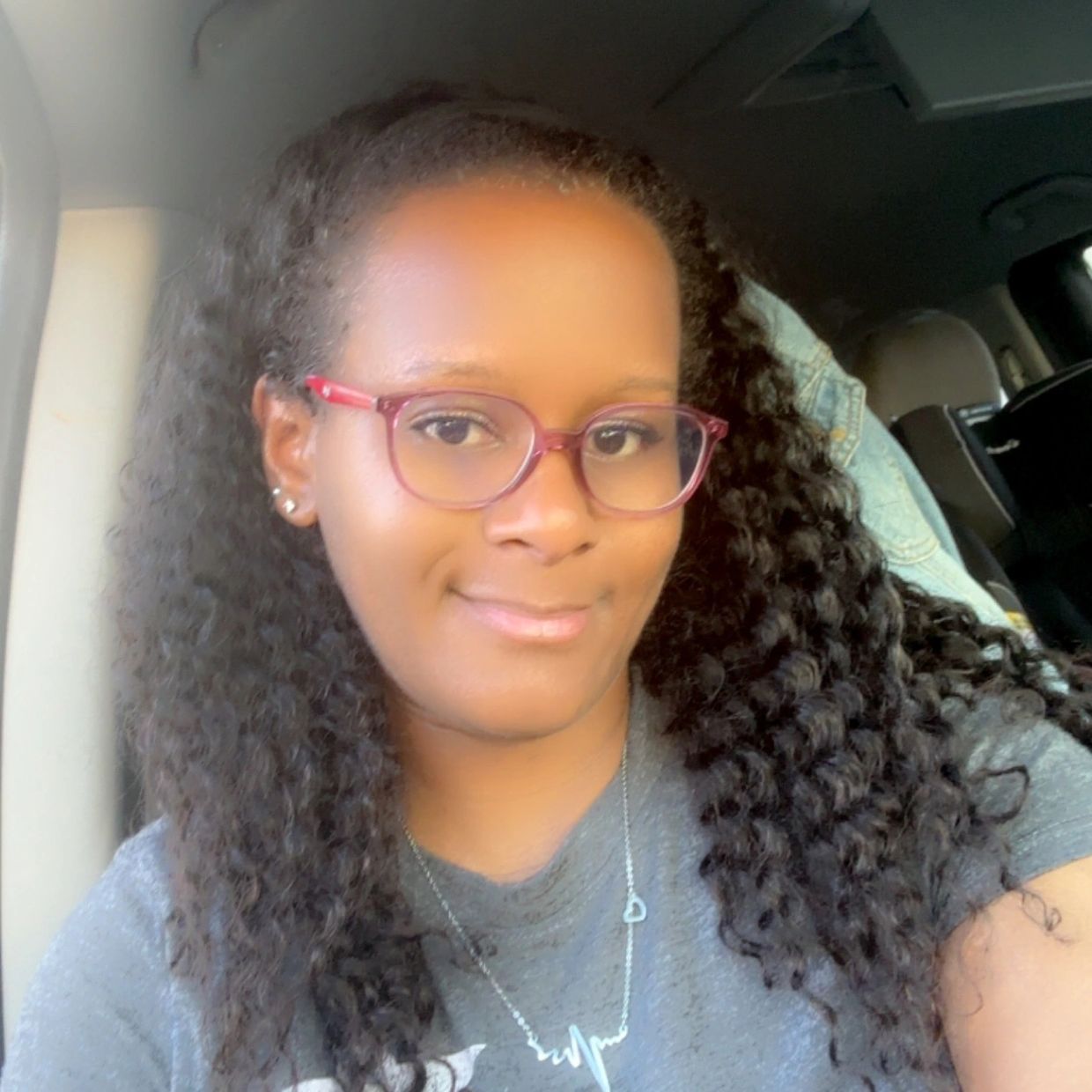 Woman with curly hair and red glasses smiling inside a car.