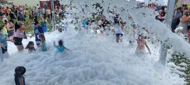 People enjoy a large outdoor foam party on a sunny day.