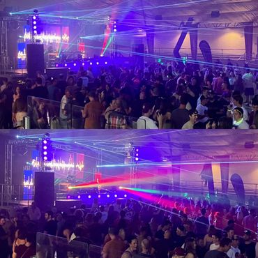 Crowded indoor concert with colorful laser lights and energetic crowd.