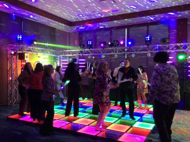 People dancing on a colorful LED-lit dance floor in a party setting.