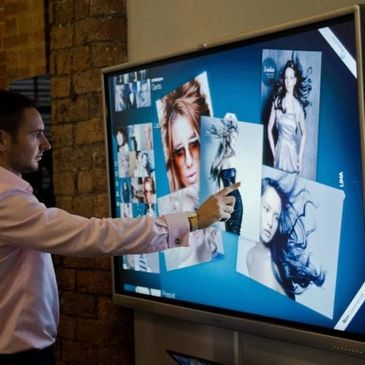 Man interacting with large touchscreen displaying photos.