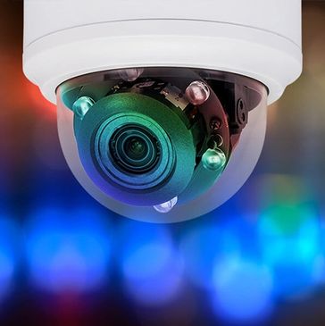 Close-up of a security camera with colorful lights in the background.