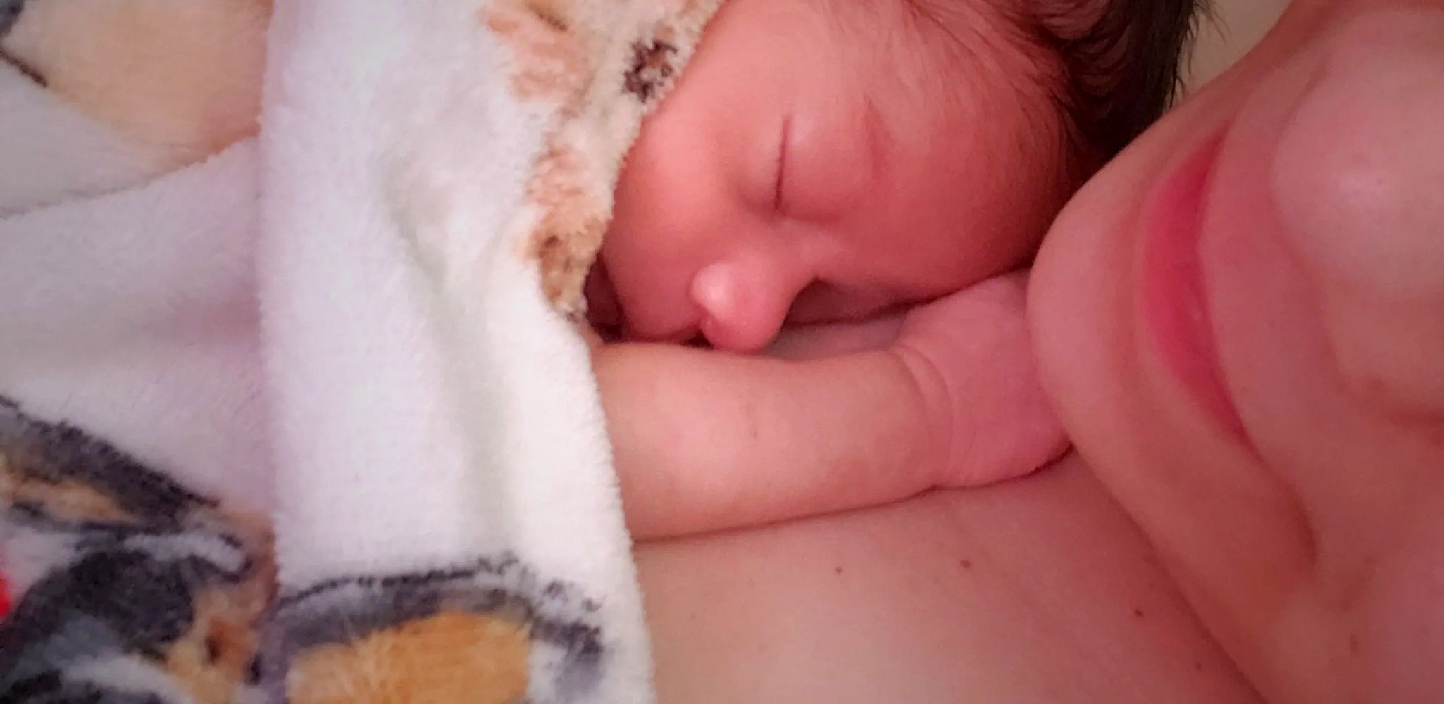 A newborn baby peacefully sleeping on mom's chest, wrapped in a soft blanket.