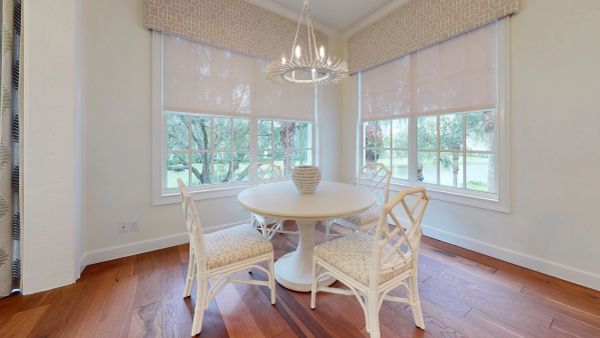 Bright dining nook with white furniture and large windows overlooking greenery.