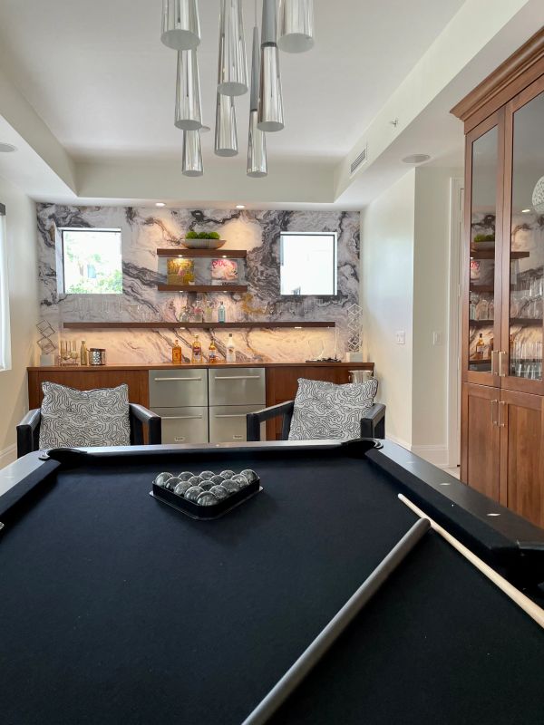 Modern game room with black pool table and stylish bar area.