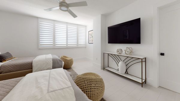 Minimalist bedroom with twin beds, woven ottomans, and a wall-mounted TV.