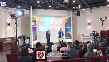 Two speakers addressing an audience in a well-lit conference room with a projector screen.