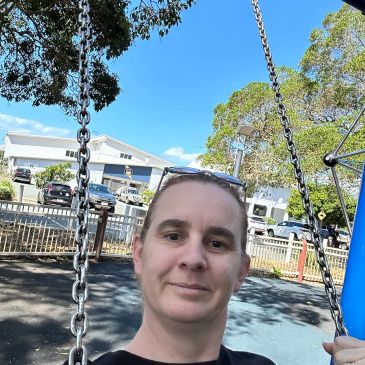 Person taking a selfie on a swing in a park.