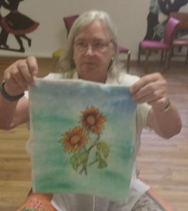 Woman proudly displays a colorful sunflower painting on fabric.