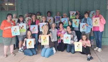 Group of women proudly displaying their sunflower paintings in a cheerful setting.