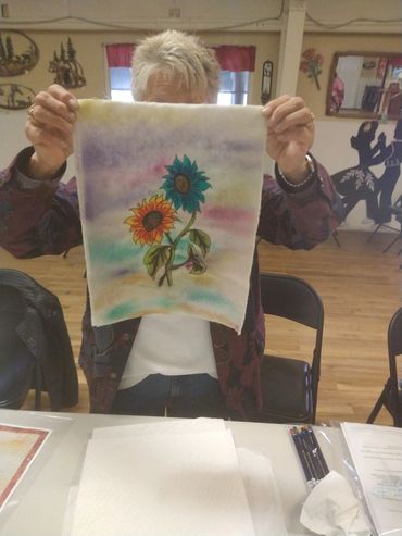 Person holding a watercolor painting of sunflowers indoors.