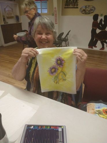 Smiling woman proudly displays her sunflower artwork.