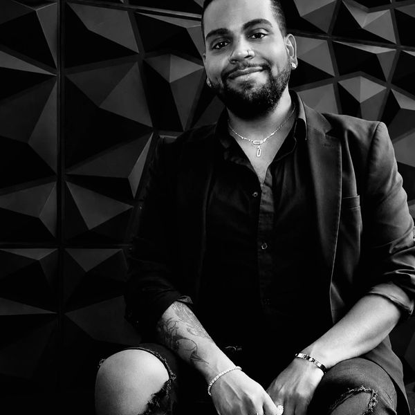 Man smiling in black jacket with ripped jeans.