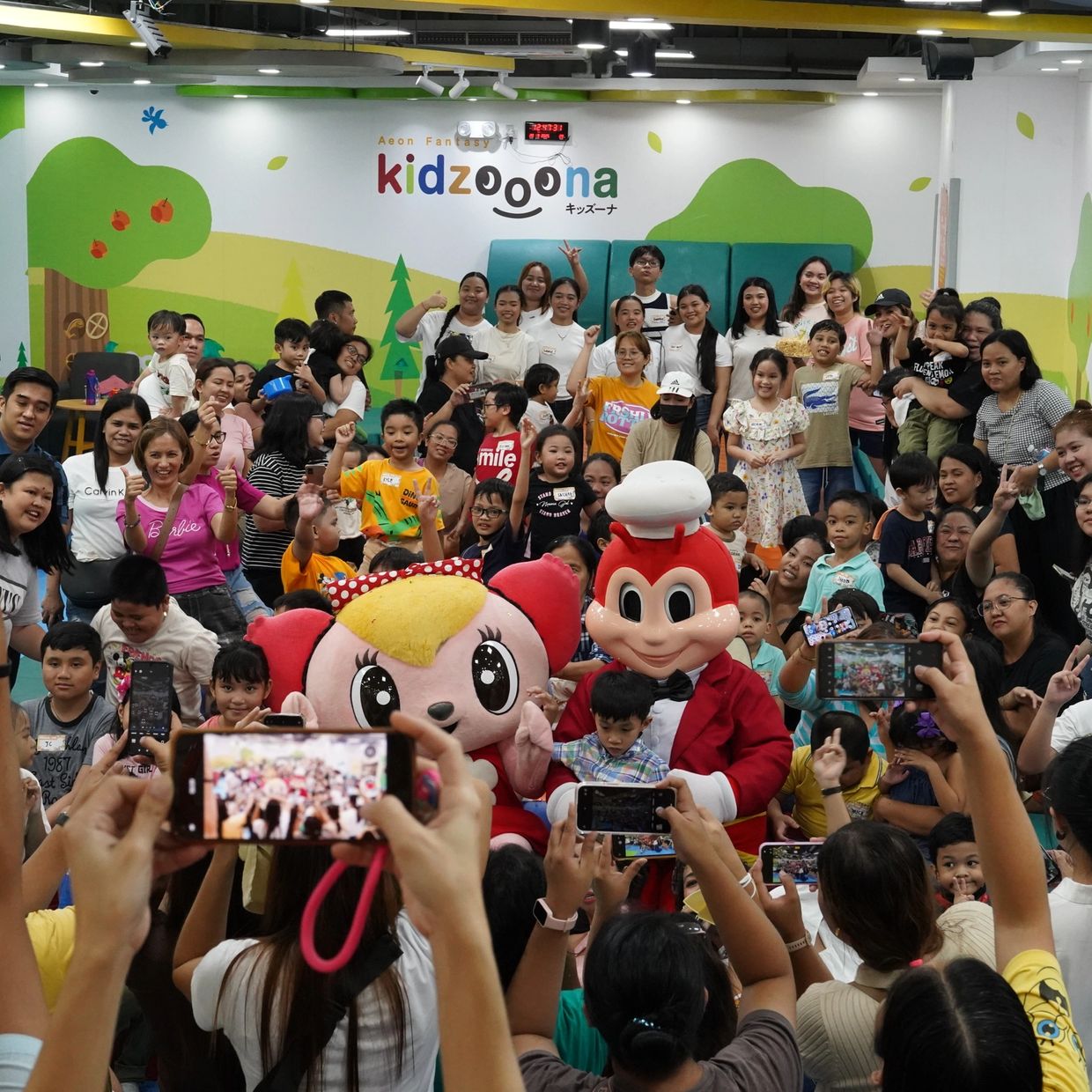 Large group of children and adults posing with mascots at Kidzoona play area.