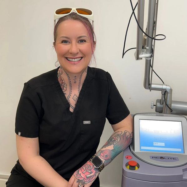 Smiling woman with tattoos and black scrubs posing by a Reolight machine.