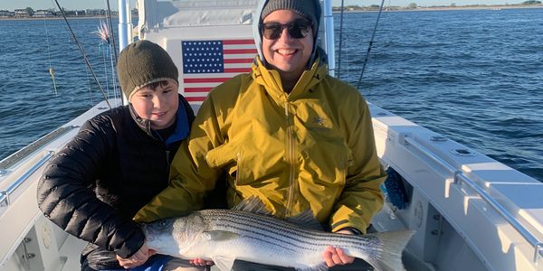 Two people on a boat holding a large striped fish they caught.