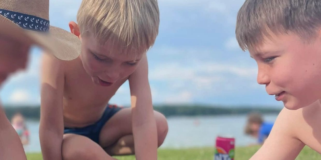 Three boys playing with toy figures on a blanket near a lake.