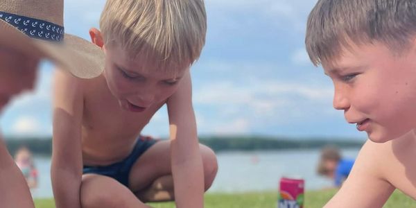 Three boys playing with toy figures on a blanket near a lake.