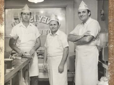 Three men wearing aprons and paper hats working in a vintage kitchen.