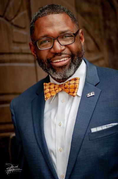 Smiling man in suit with bow tie and glasses.