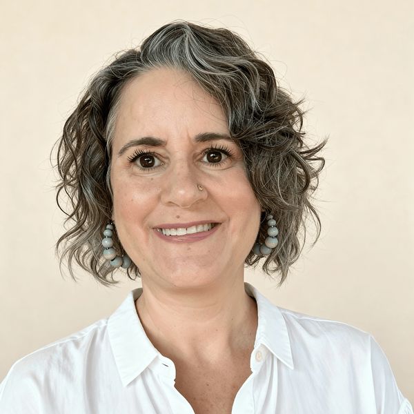 Smiling woman with curly gray hair and blue earrings.