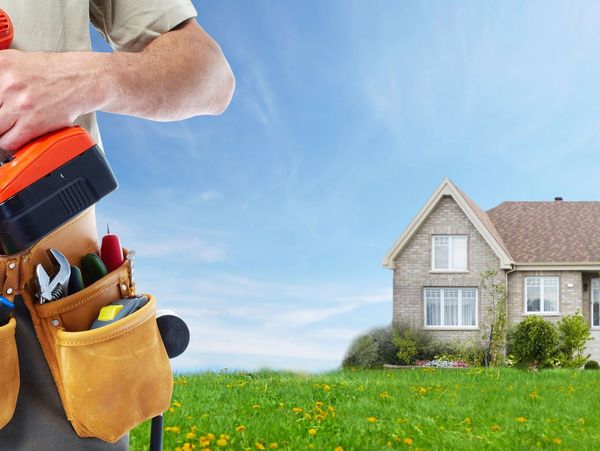 Picture of a handyman with his tool belt standing in front of a house.