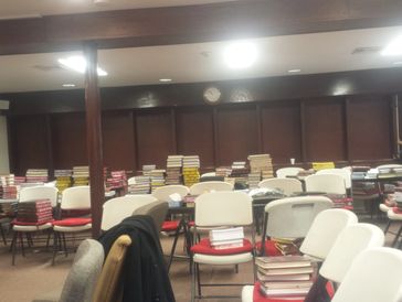 Classroom filled with stacks of books on chairs and desks.