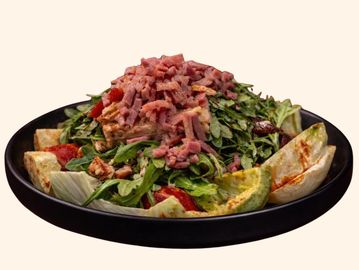 Fresh salad topped with chopped ham on a black plate.