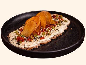 Gourmet dish with creamy spread, diced vegetables, and crispy chips on a black plate.