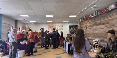 People browsing and shopping at a local indoor market with a 'PEACE' sign on the wall.