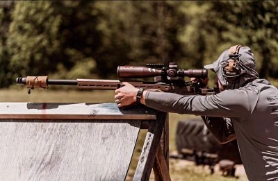 Person aiming a sniper rifle outdoors.