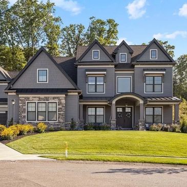 Large two-story gray house with stone accents and a manicured lawn.