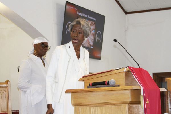 Two elderly women in white standing near a podium in a church.