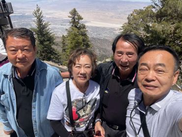 Four adults smiling outdoors with scenic mountain and valley views behind them.
