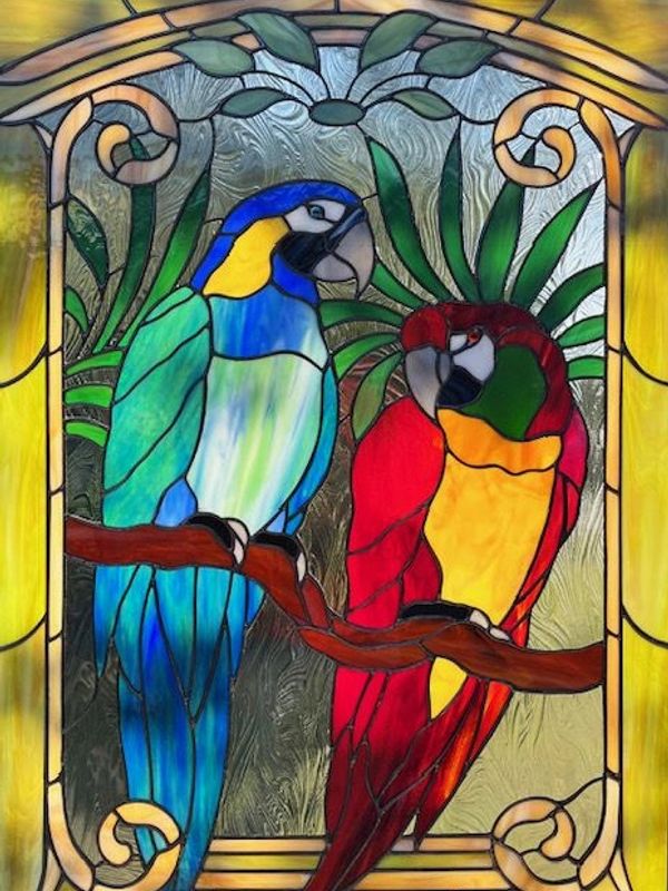 Stained glass artwork of two colorful parrots perched on a branch.