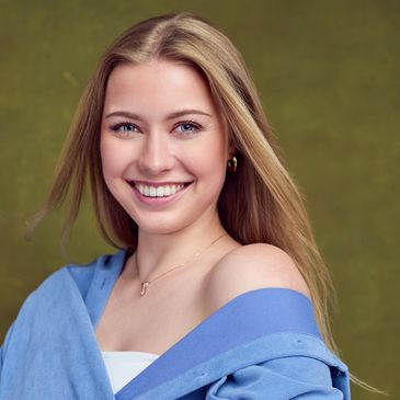 Smiling young woman with blonde hair wearing a blue off-shoulder top.